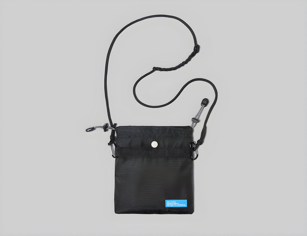 Small dark crossbody bag with adjustable strap, front snap button, and small label