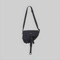 Black single-strap crossbody sling bag with front flap and hanging tie detail