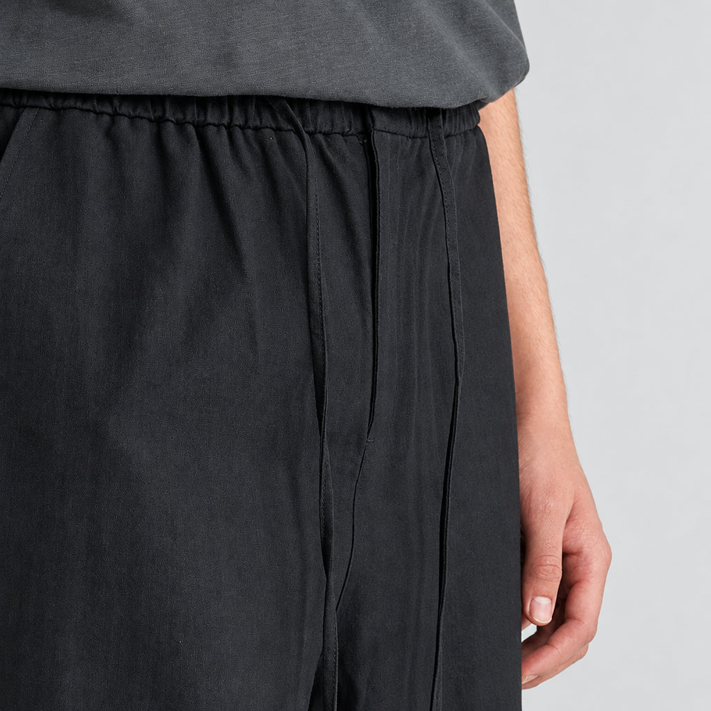 Black linen-blend wide-leg trousers close-up of elastic waistband and pleated front