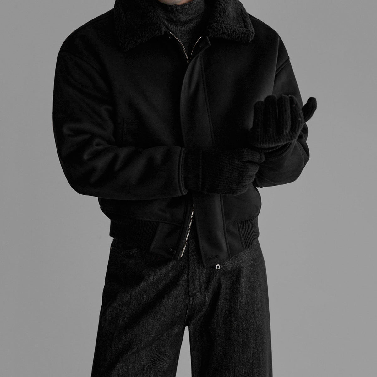 Black flight jacket close-up with zip, fleece collar, and ribbed sleeve cuffs